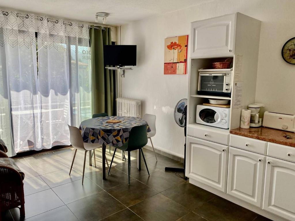 une cuisine avec une table avec des chaises et un micro-ondes dans l'établissement Studio cosy 24 m² avec balcon, proche cures et centre-ville, animaux bienvenus ! - FR-1-703-109, à Amélie-les-Bains-Palalda