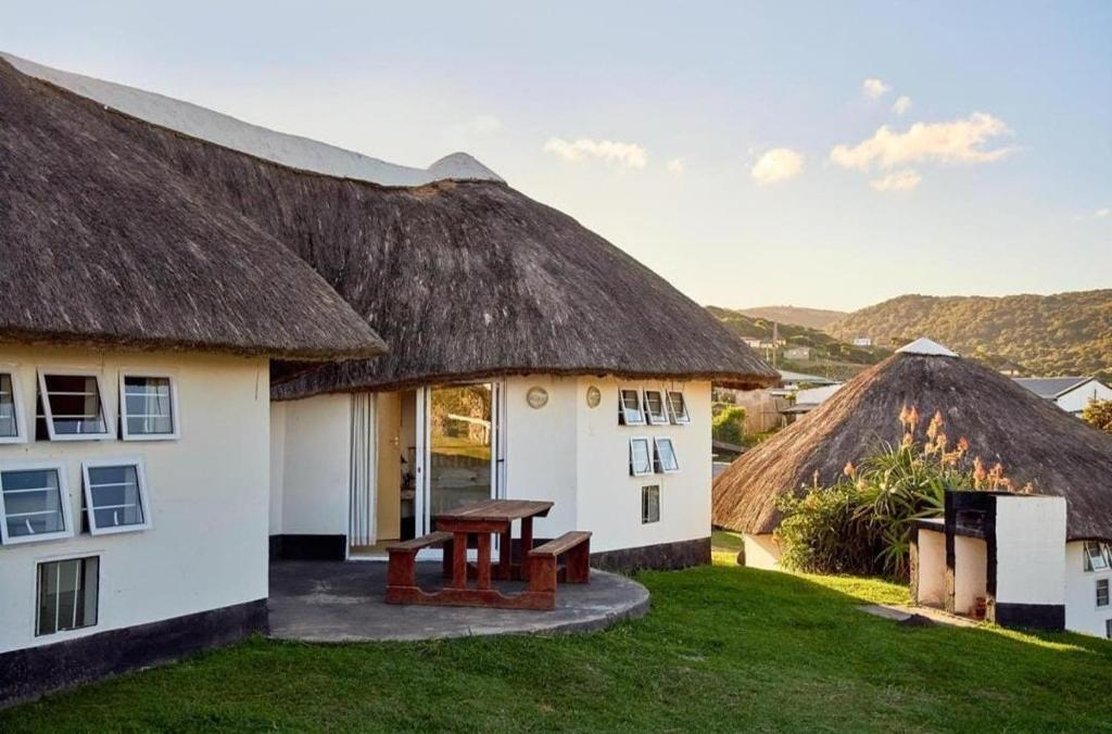 a house with a thatched roof with a picnic table at Hole in the Wall - Unit 47 in Coffee Bay