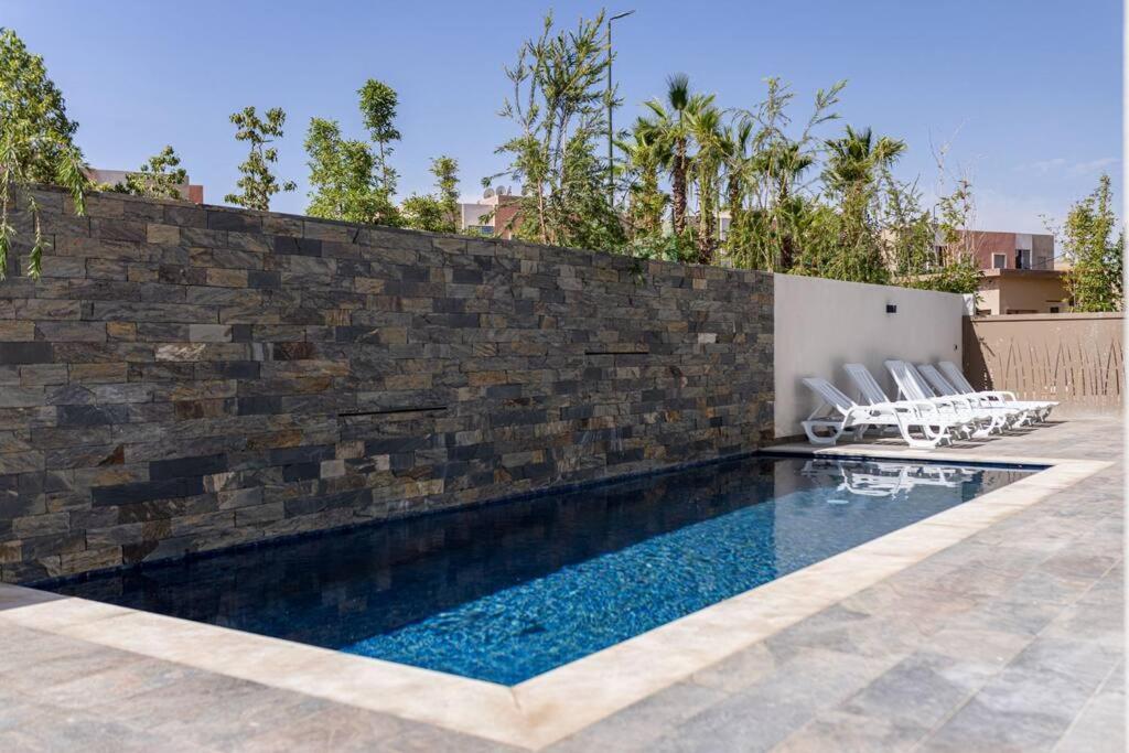 uma piscina com cadeiras ao lado de uma parede de tijolos em Marrakech villa avec piscine privée 4 chambres 4 salles de bains em Marrakech