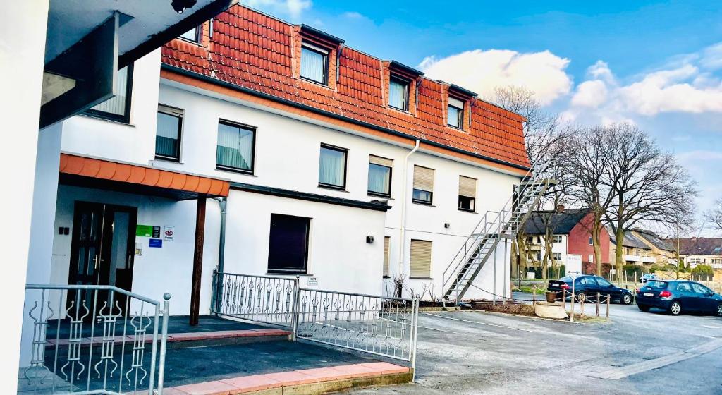 een wit gebouw met een rood dak en een parkeerplaats bij Pension Alex in Bielefeld