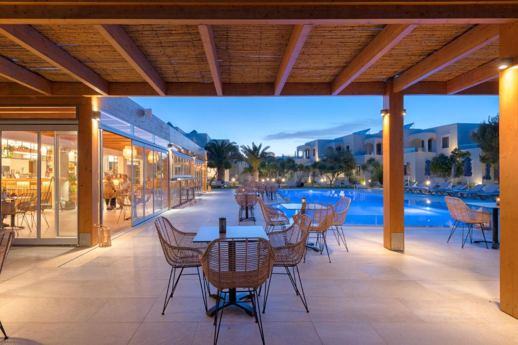 a patio with tables and chairs next to a swimming pool at Malena Hotel & Suites - Adults Only by Omilos Hotels in Amoudara Herakliou