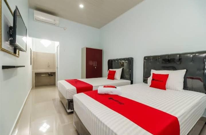 duas camas num quarto com vermelho e branco em RedDoorz Plus near Palembang Icon Mall 2 em Palimbão