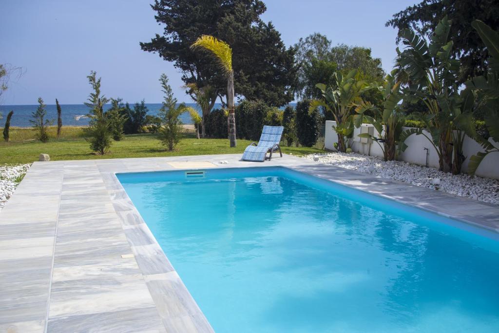 a blue swimming pool with a chair and the ocean at Katerina House in Perivolia