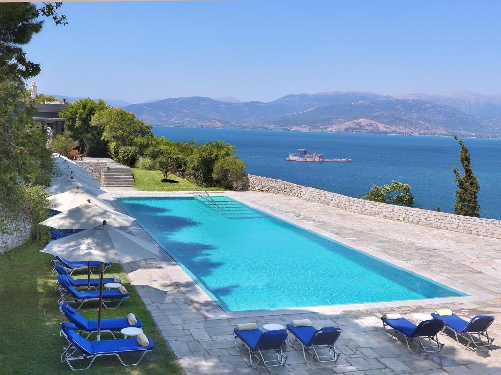 a swimming pool with chairs and umbrellas and the water at Nafplia Palace Hotel & Villas in Nafplio