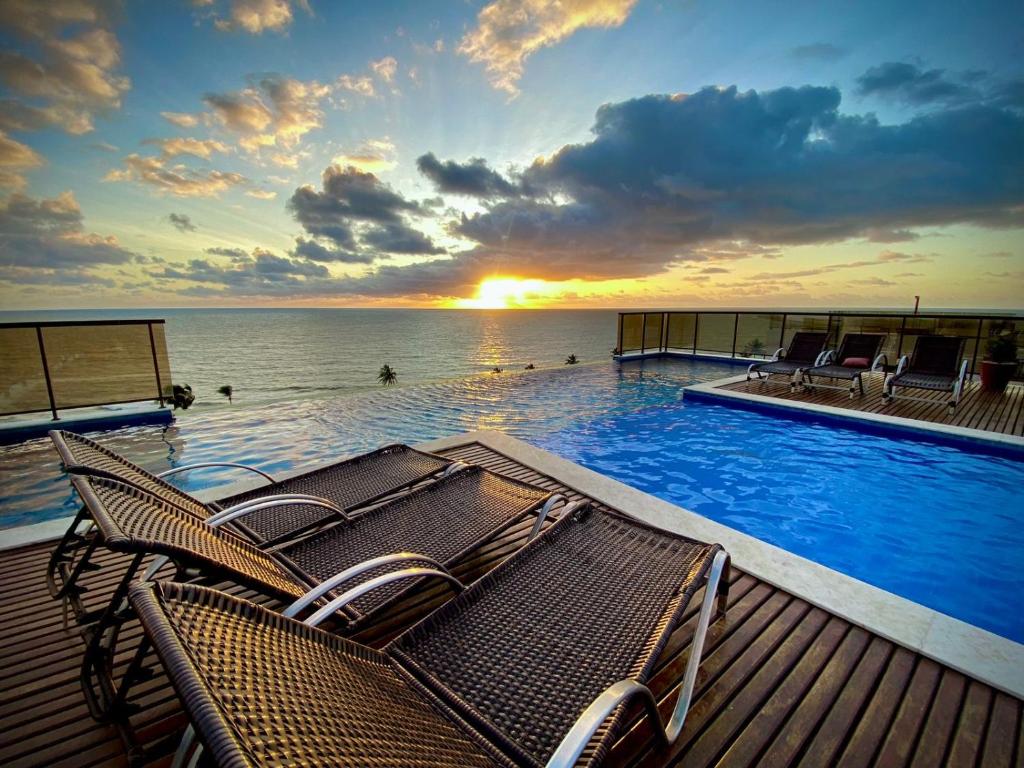 a swimming pool with chairs and the ocean at sunset at Maravilhoso local para aproveitar e descansar in Conde