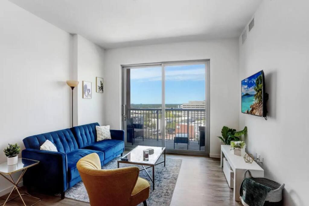1BR Oasis in Downtown Tampa w Balcony & City Views في تامبا: غرفة معيشة مع أريكة زرقاء ونافذة كبيرة