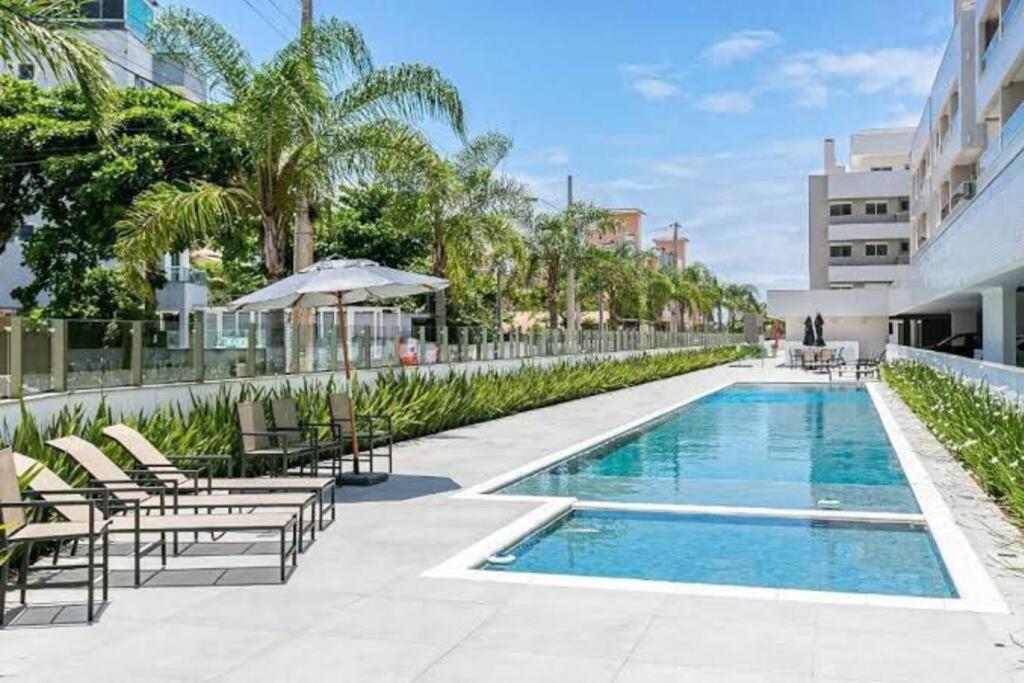 uma piscina com cadeiras e um guarda-sol ao lado de um edifício em Lindo apt Garden Cannes Club em Florianópolis