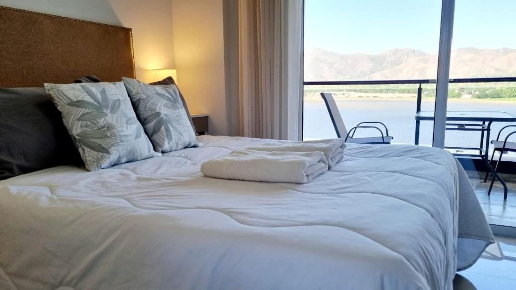 a white bed in a room with a large window at Departamento frente a lago Carlos Paz - Villa Siquiman - Complejo Veneto Village in Villa Parque Siquiman