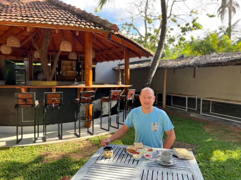 a man sitting at a picnic table with food on it at PineApple Surf in Ahangama