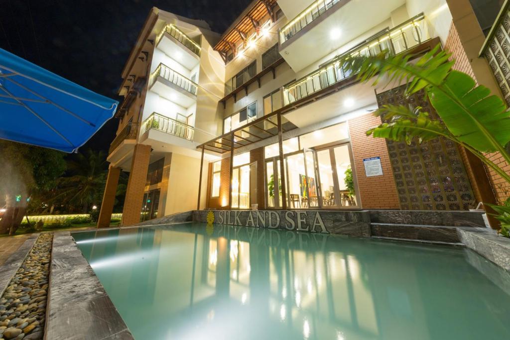 uma piscina em frente a um edifício à noite em Silk and Sea Hotel em Hoi An