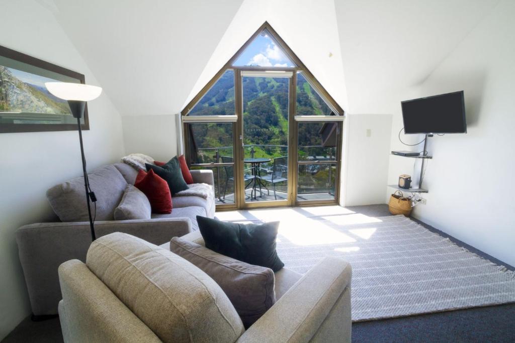 a living room with two couches and a large window at Lantern 1 Bedroom Balcony with Panoramic Alpine View in Thredbo