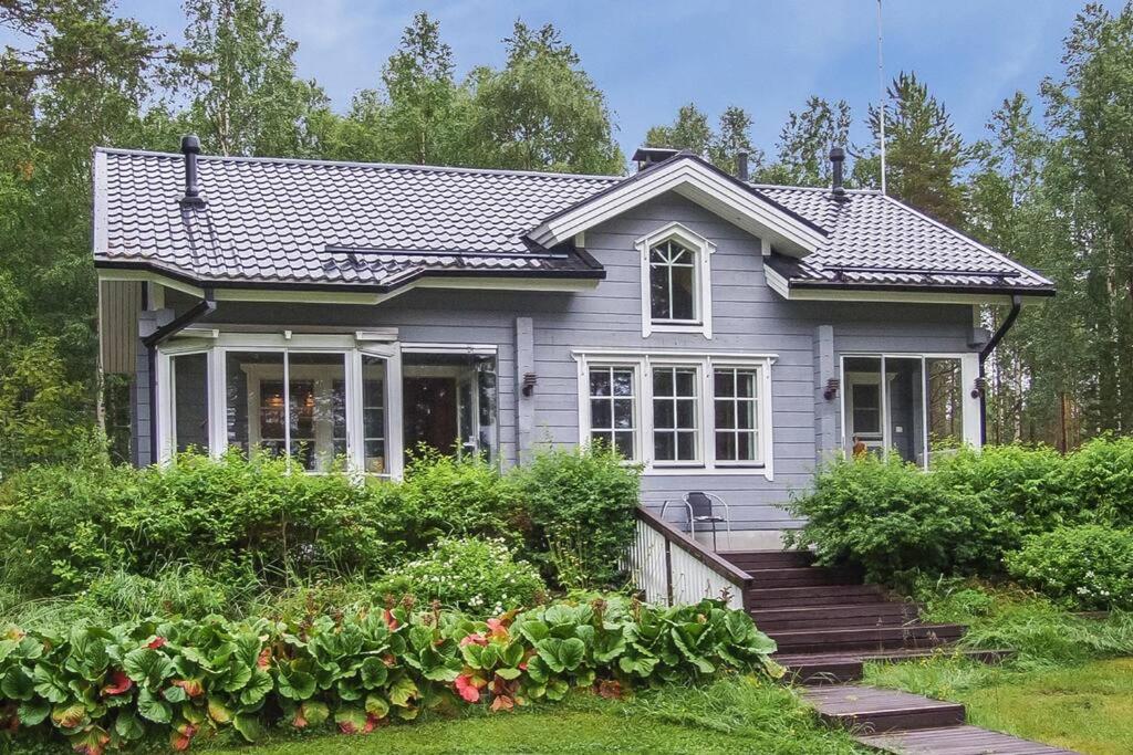 a small gray house with a porch and some bushes at Villa Ojala, a lovely cottage with own beach in Kuusamo
