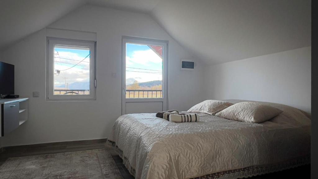 a white bedroom with a bed and two windows at Seoski kutak Piva in Plužine