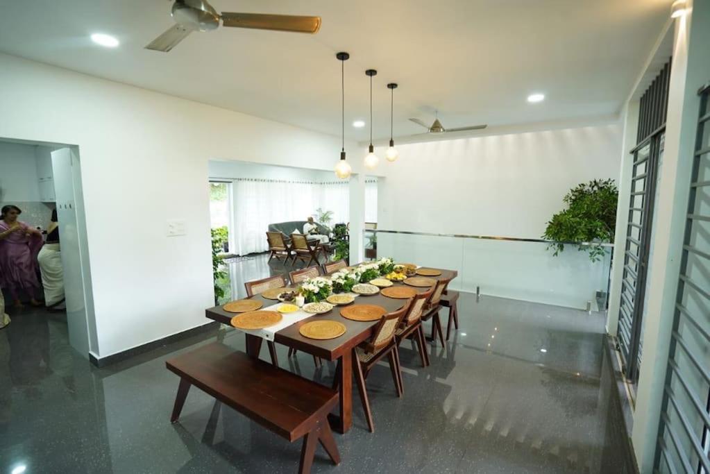uma grande sala de jantar com uma mesa longa e cadeiras em Ultra Modern Glass house with large Swimming pool and garden em Kottayam
