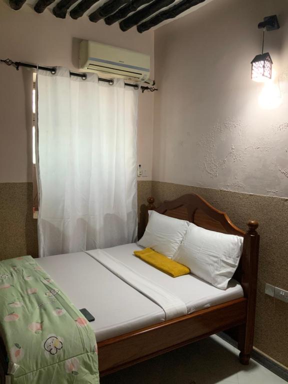 a bedroom with a bed with white sheets and a window at Zebra House III StoneTown in Ngambo