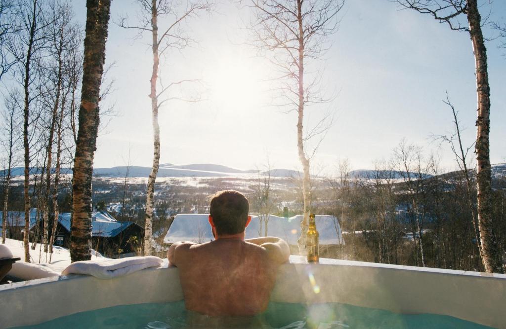 um homem sentado numa banheira de hidromassagem com vista para as montanhas em Fjällfrid stugby em Bruksvallarna