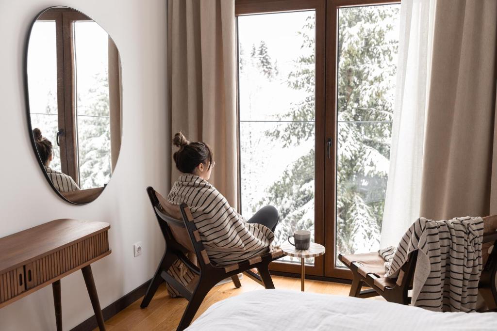 a woman sitting in a chair looking out of a window at Glečer Kop, Cozy design apartment A5 in Kopaonik