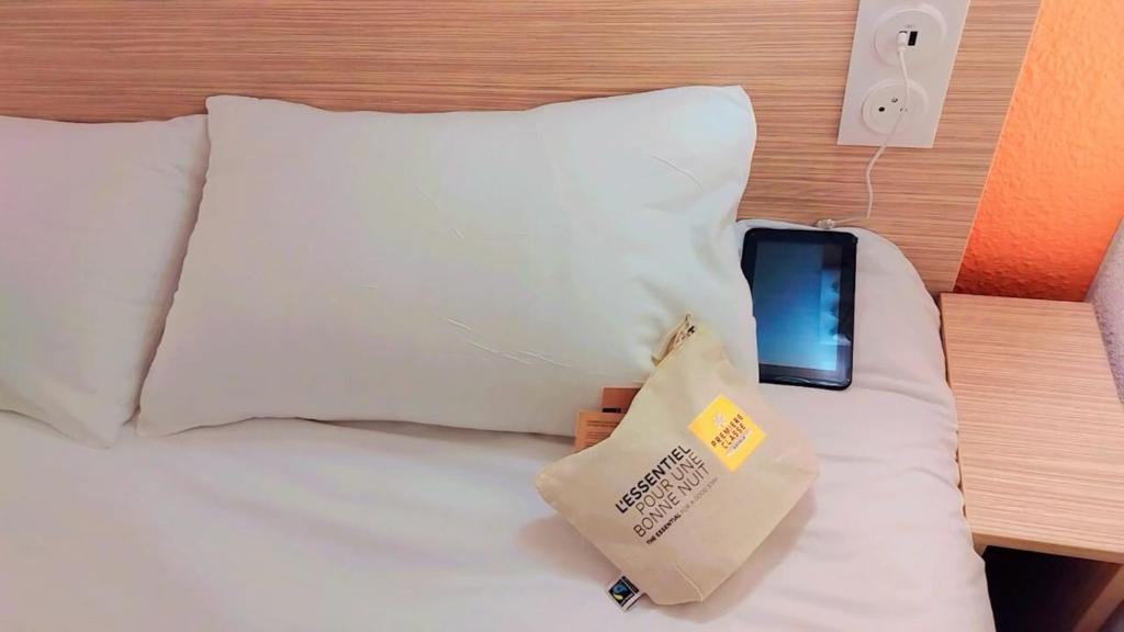 a bed with a cell phone and a bag on it at Premiere Classe Troyes Sud - Parc St Thibault in Isle-Aumont
