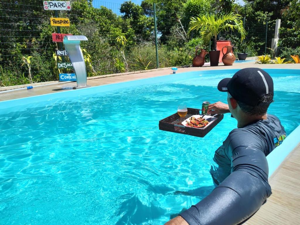 un homme dans une piscine avec un plateau de nourriture dans l'établissement Casa de ferias paraíso, à Santa Cruz Cabrália