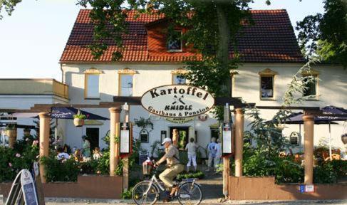 um homem a andar de bicicleta em frente a um restaurante em Kartoffelgasthaus & Pension Knidle em Lübbenau