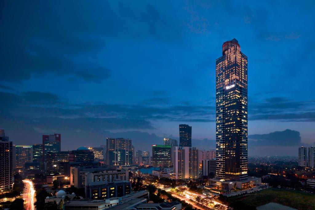 une vue sur la ville la nuit avec un haut gratte-ciel dans l'établissement The Westin Jakarta, à Jakarta
