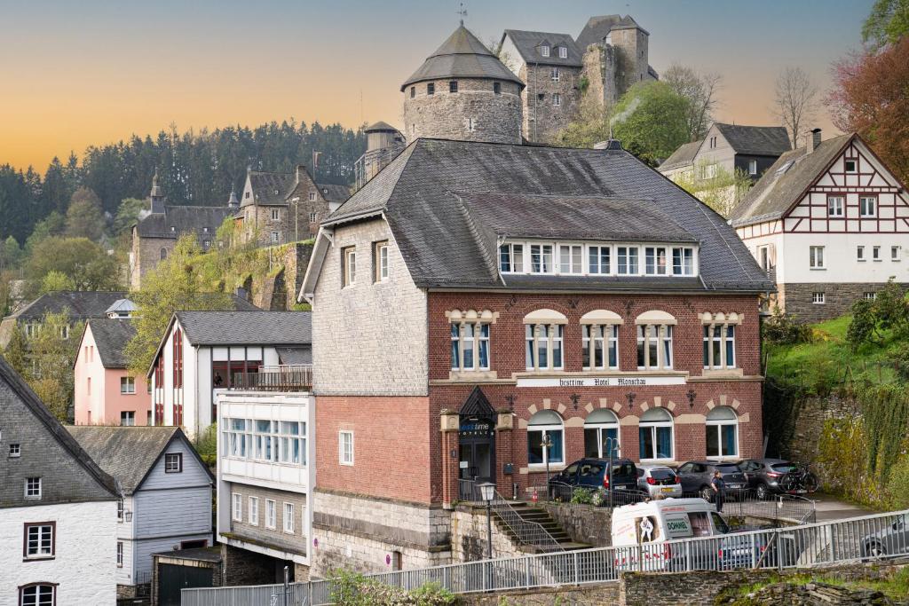 un grand bâtiment en briques avec un château en arrière-plan dans l'établissement besttime Hotel Monschau, à Monschau