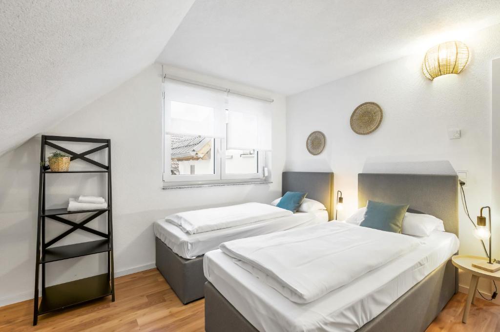 2 camas en una habitación con paredes blancas y ventana en Sali Homes - Residenz zum Breitenauer See, en Obersulm