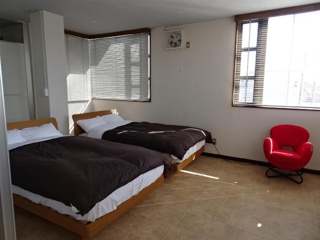 1 dormitorio con 2 camas y silla roja en Corpo Umeyama 2F / Vacation STAY 4853, en Mibu
