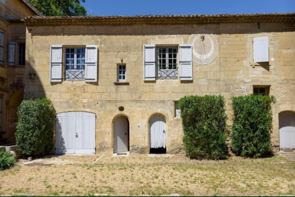 uma antiga casa de pedra com portas brancas e arbustos em Château Teillan - Cadran solaire em Aimargues
