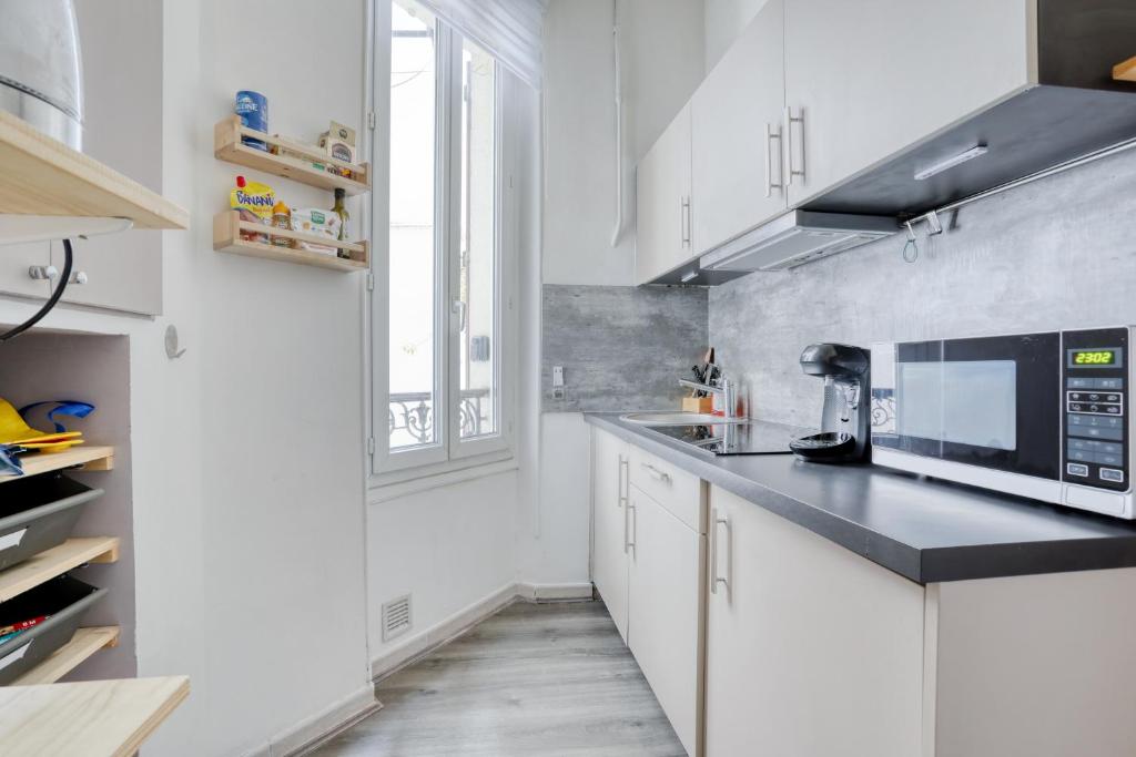 a kitchen with white cabinets and a black counter top at Chic Appartement Climatisé à 10 Minutes de Paris: Confort et Élégance in Maisons-Alfort
