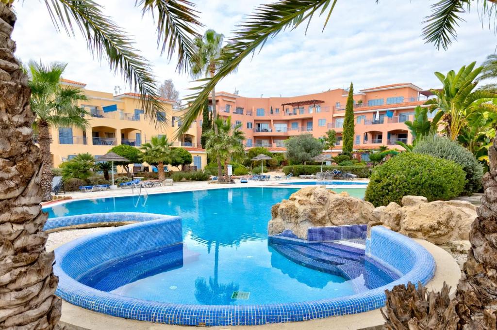 a pool at a resort with palm trees at Limnaria Gardens Cozy Apartment in Paphos City