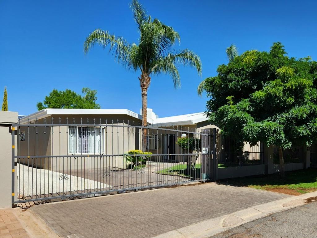 a fence in front of a house with a palm tree at Green Kalahari Guesthouse in Upington