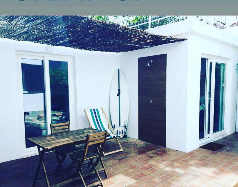 een patio met een tafel en stoelen en een surfplank bij Hoso Loft 24 Beach House in Costa da Caparica