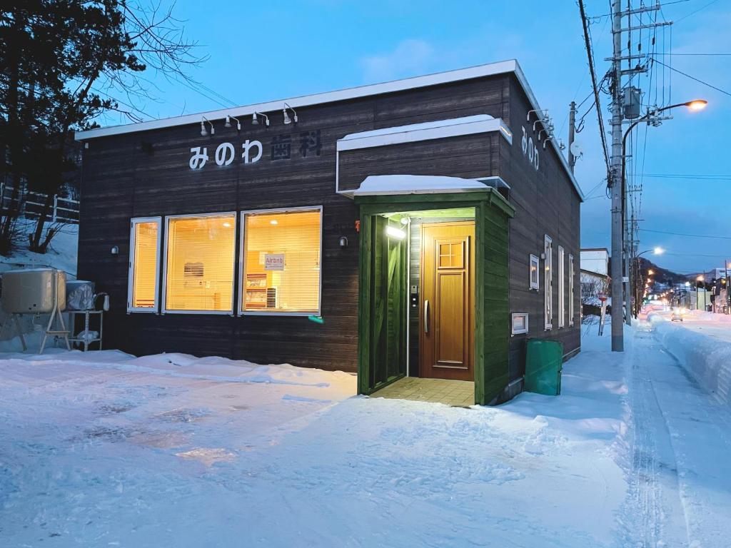 un pequeño edificio con una puerta verde en la nieve en Minowa airbnb en Yubari