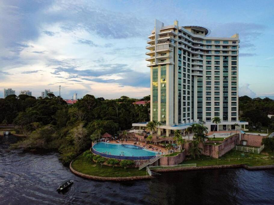 a large building with a swimming pool next to a river at Flat em Tropical executive Hotel in Manaus