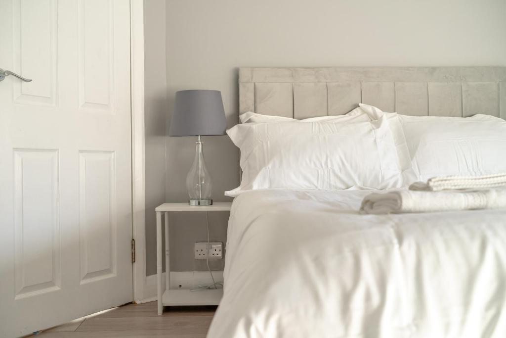 Enjoy a Luxury & Peaceful Home in Loughton, Essex في لوثيون: سرير بملاءات بيضاء ومصباح على طاولة