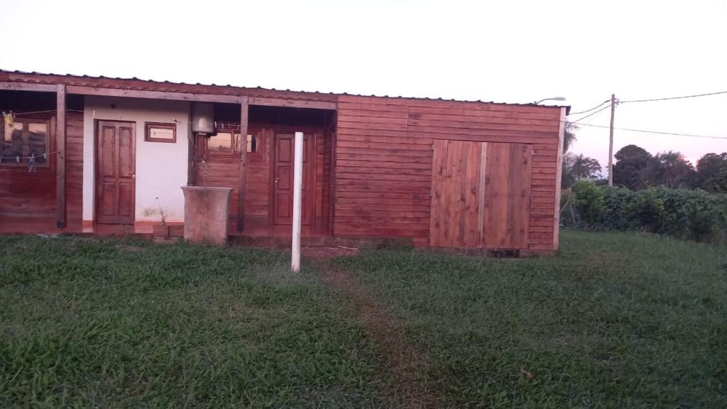 a small wooden house with a door and a grass field at LA CABAÑA DE SERGIO in Gobernador Roca