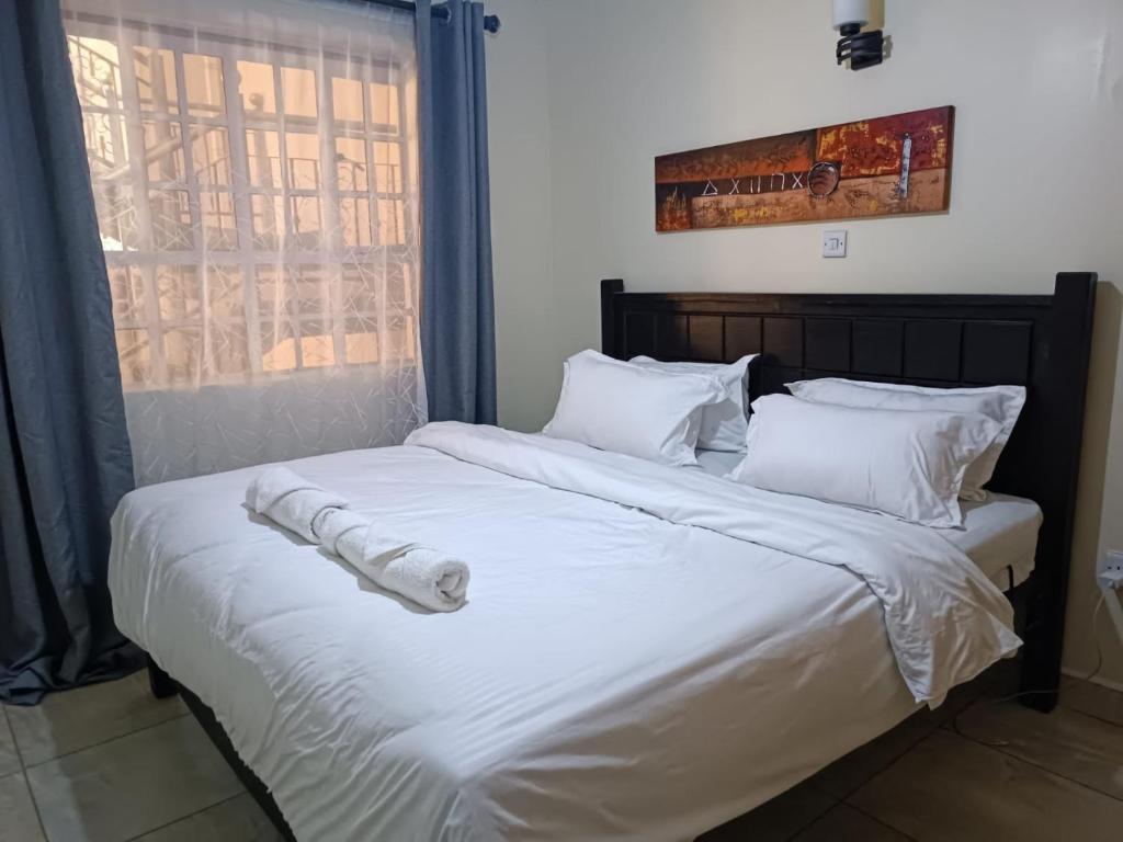 a large bed with white sheets and pillows at Lux Suites Neema Court Furnished Apartments in Nairobi