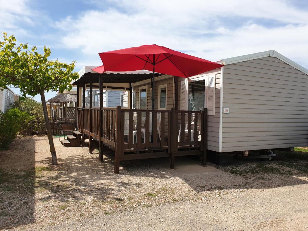 a house with a deck with a red umbrella at Mobile-home les pieds dans l'eau in Palavas-les-Flots