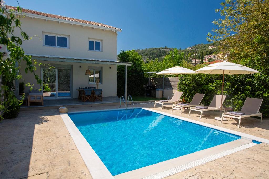 a swimming pool in front of a house with umbrellas at Grappolo Lefkada Villas - Athiri, 5 min from wonderful Ai Giannis beach & Lefkada town in Apolpaina