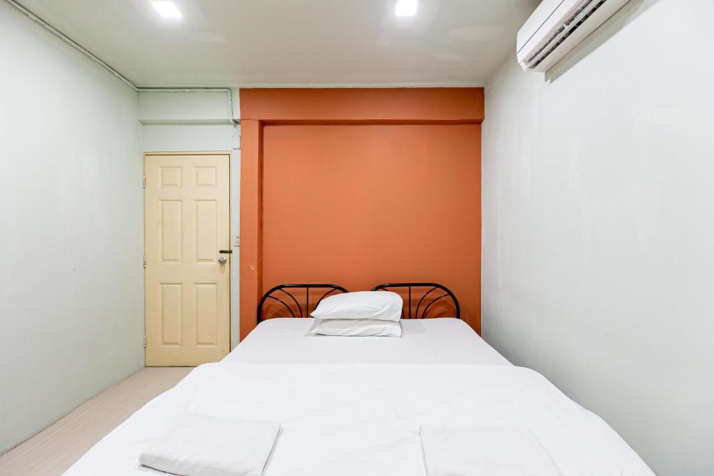 Freesia Saladaeng Silom Apartments في بانكوك: غرفة نوم صغيرة مع سرير أبيض وجدار برتقالي