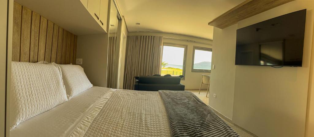 1 dormitorio con 1 cama, TV y silla en Ágape Suítes & Apartamentos en São Sebastião