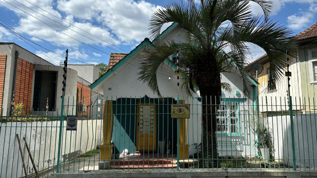 a house with a palm tree in front of a fence at Hostel Hug Brasil in Curitiba