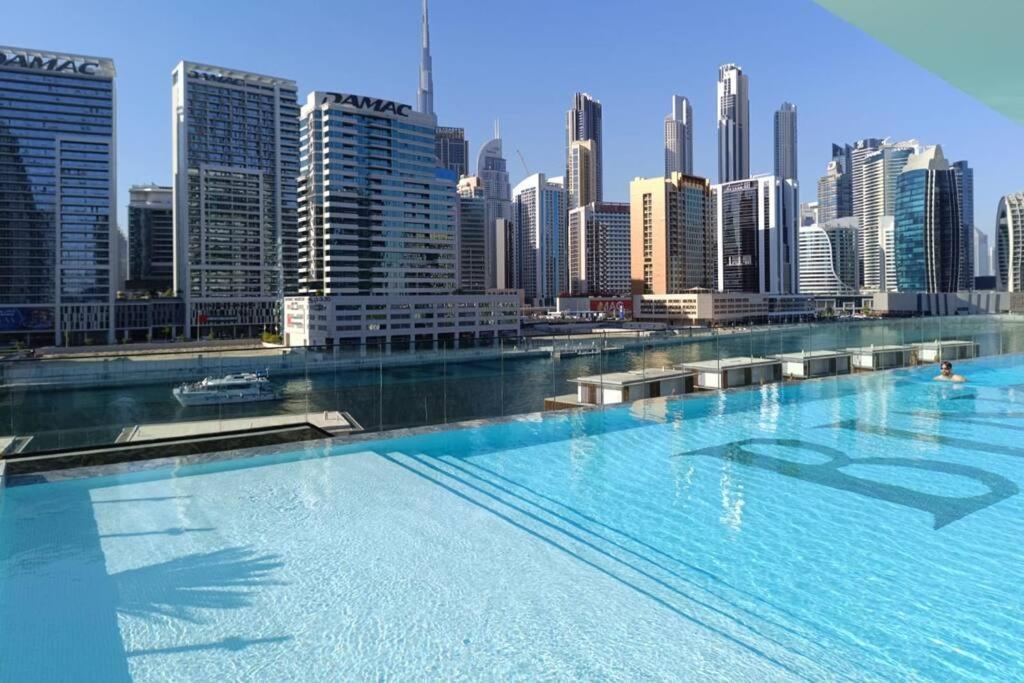 a large swimming pool in front of a city at 1BR Canal View 10 min to Dubai Mall & Burj in Dubai