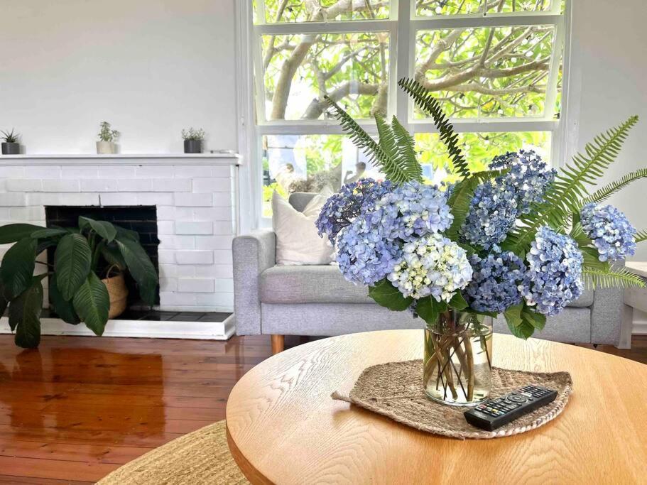 een vaas met blauwe bloemen op een tafel in een woonkamer bij Sandon Beach Cottage in Bulli