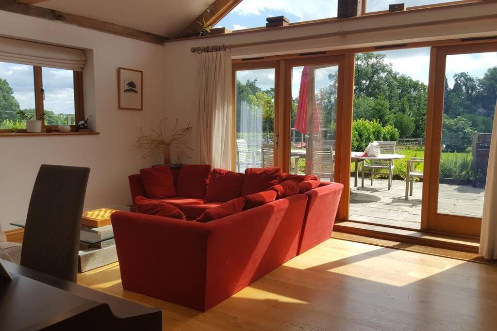 a living room with a red couch and a table at Prestwick Oak - Sleeps 10 - Rural Oak Frame Barns in Chiddingfold