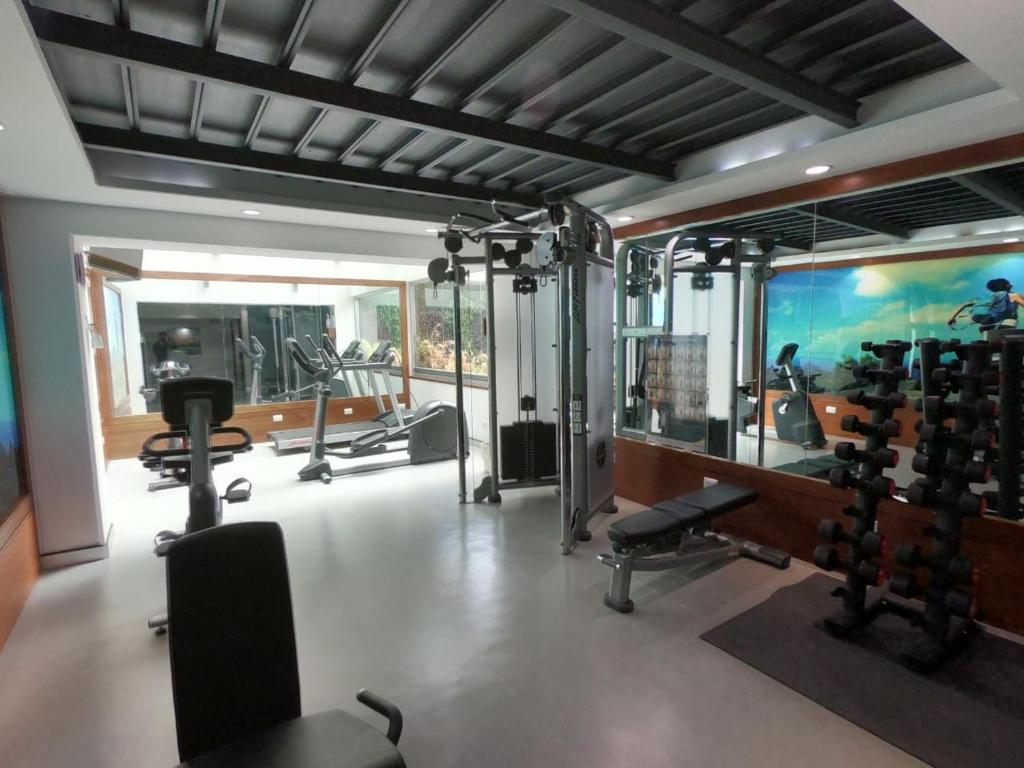 A bright fitness room with cardio machines, a cable station, free weights and a bench.