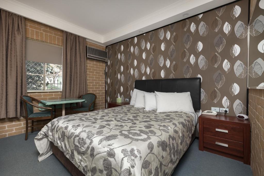 a bedroom with a bed and a table and a window at Grand Manor Motor Inn in Queanbeyan