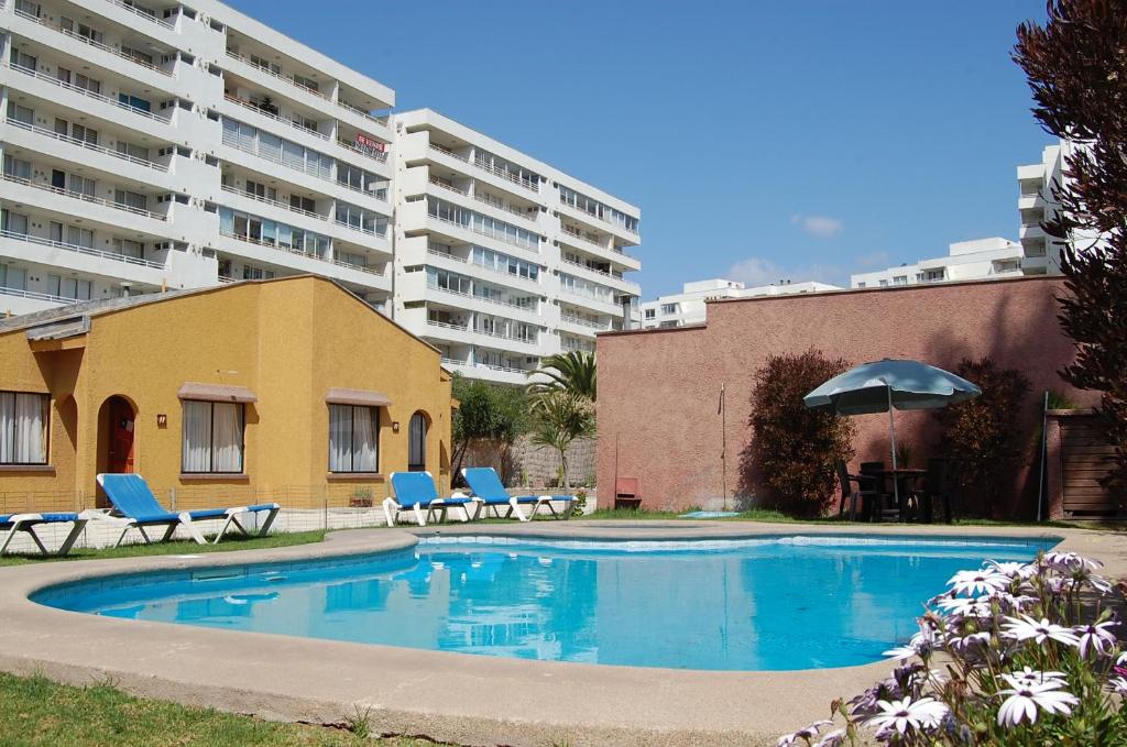una piscina con sillas, sombrilla y edificios en De La Costa Cabañas, en La Serena