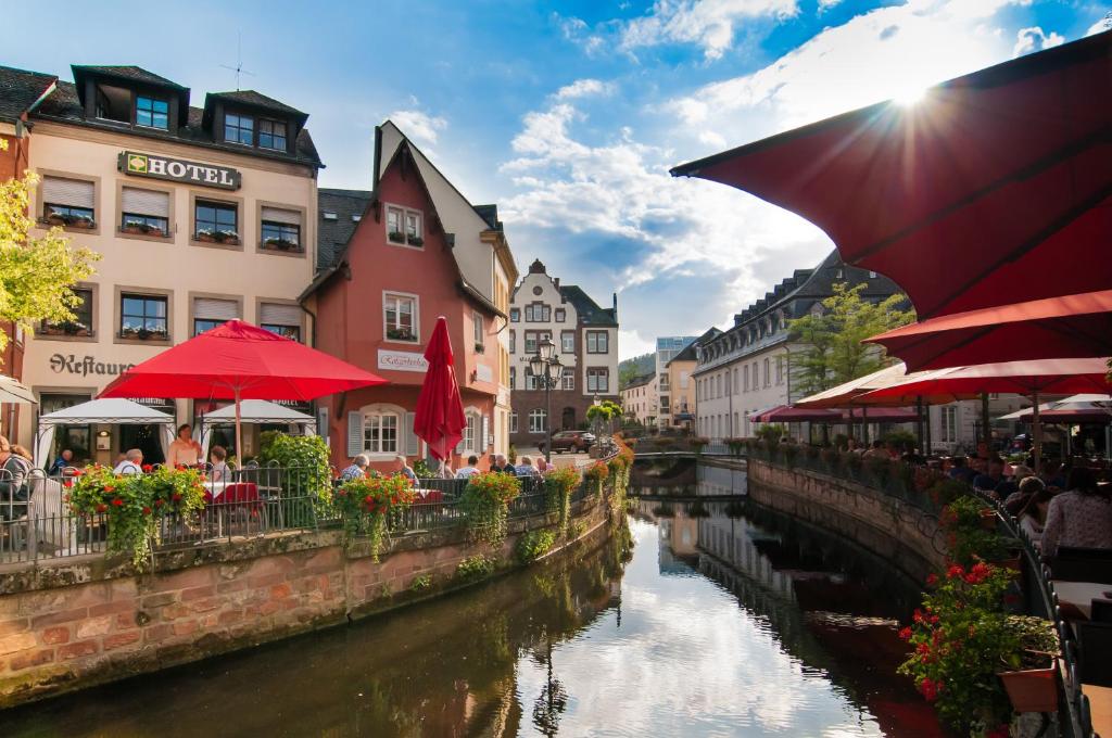 a river with tables and umbrellas next to a canal at Hotel Restaurant Zunftstube in Saarburg